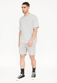 Lys grå t-shirt med korte ærmer, rund halsudskæring og subtil branding. Parret med lys grå shorts og sorte højhalsede sneakers.