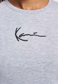 T-shirt in cotone grigio con design del logo ricamato in nero sul davanti, scollatura rotonda e maniche corte.