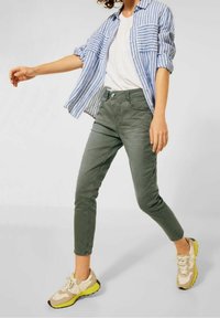 Pasiasta niebiesko-biała koszula, biała koszulka, oliwkowe spodnie, beżowe i żółte sneakersy. Casualowy strój, lekki materiał, luźny krój.