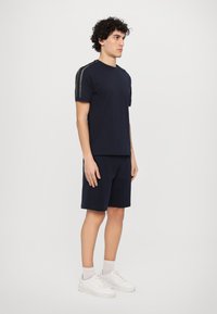 Camiseta de manga curta azul-marinho com detalhes em listras contrastantes nos ombros, combinada com calções a condizer e sapatilhas brancas.