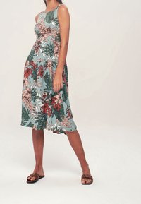 Ärmelloses Kleid mit Blumenmuster, enganliegendem Oberteil und ausgestelltem Rock. Es zeigt grüne, pinke und rote Motive auf einem hellblauen Hintergrund.