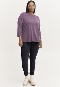 Lila oversized tröja med trekvartslånga ärmar, tillsammans med svarta slim-fit byxor och beige ankelstövlar. Mjuk textur, minimalistisk design.