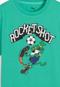 Maglietta verde con pantera dei cartoni animati in uniforme da calcio che calcia un pallone infuocato sotto il testo "ROCKET SHOT" in caratteri grassetto.