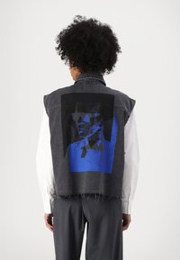 Denim jopica v temno sivi barvi z raztrganim robom. Ima izrazit modro-črni grafični potisk na hrbtni strani. Brezrokaven dizajn s ovratnikom.
