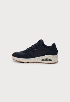 Baskets Skechers bleu marine avec semelle blanche et coussin d'air visible, lacets sur le devant, et semelle marron sur un fond uni.