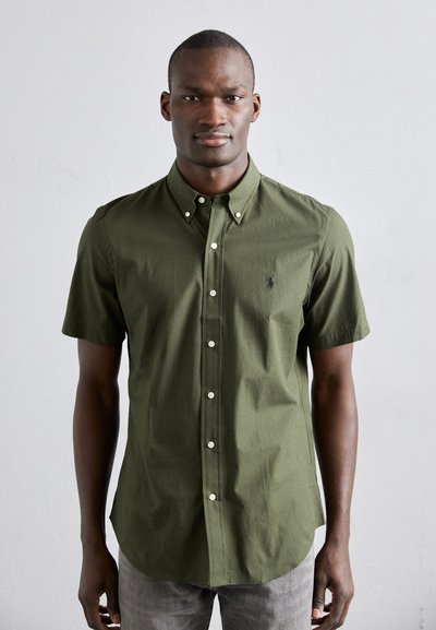Chemise à manches courtes, olive, en coton avec une coupe décontractée. Dotée de boutons blancs et d'un petit logo brodé sur la poitrine.