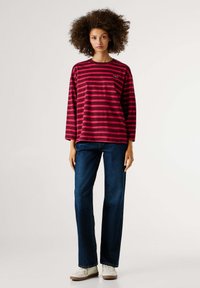 Crvena i ružičasta prugasta majica dugih rukava uparena s plavim trapericama ravnog kroja, upotpunjena bijelim tenisicama. Ležerni, udoban kroj s rebrastim ovratnikom.