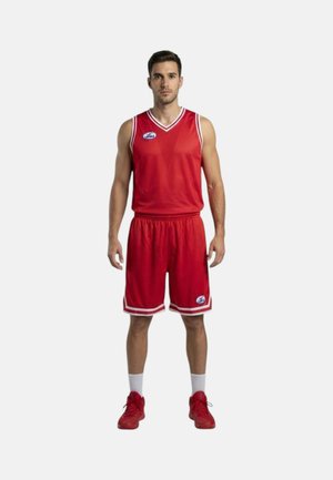Uomo in piedi che indossa una maglia da basket rossa, pantaloncini abbinati, calzini bianchi e scarpe da basket rosse su uno sfondo uniforme.