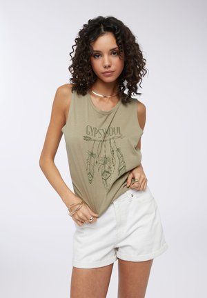 Top senza maniche verde oliva con stampa "GYPSY SOUL" e grafiche di piume, abbinato a pantaloni corti di jeans bianchi arrotolati, con una vestibilità rilassata.