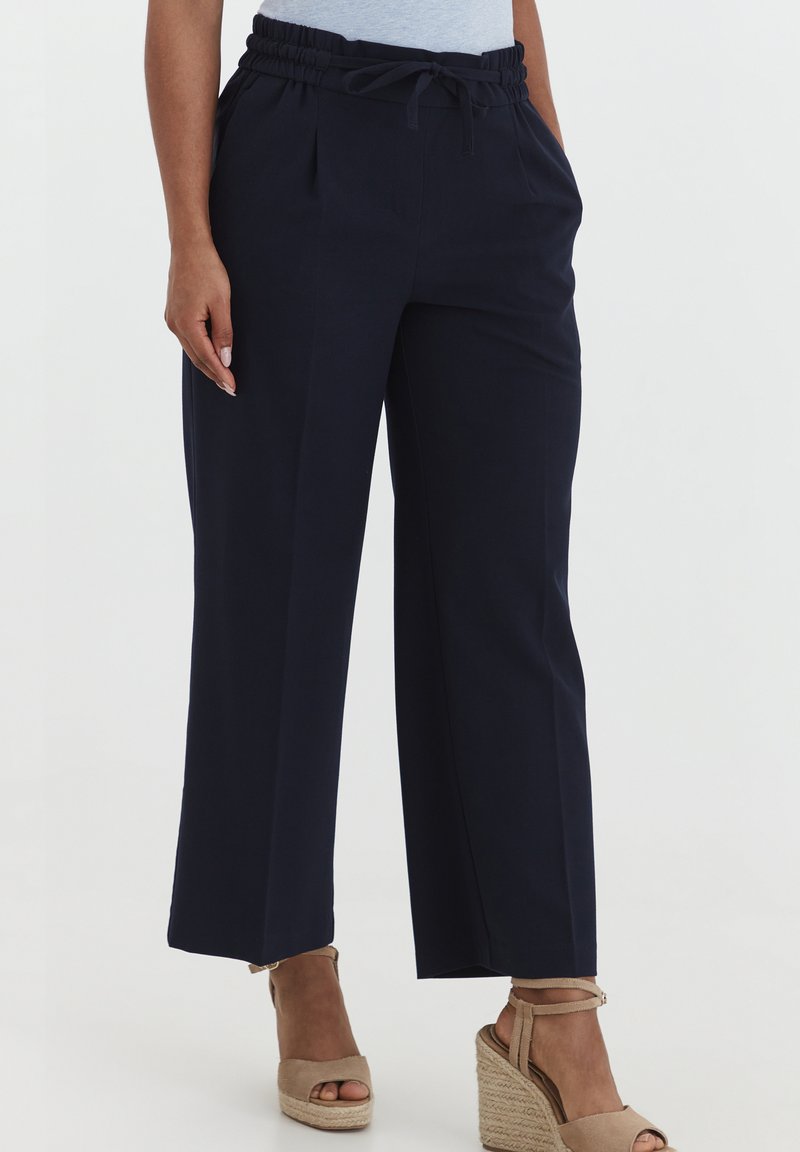 Navy trousers with a relaxed fit, elastic waistband, and drawstring. Fabric is smooth with side pockets and wide, straight legs.