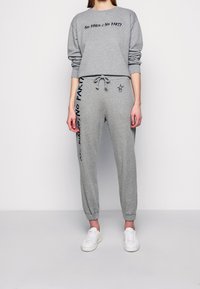 Grijze sweatshirt met de tekst "No PINKo No PARTY", gecombineerd met bijpassende joggers met zijprints en een trekkoord in de taille. Witte sneakers maken de look compleet.