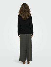 Maglione nero lavorato a maglia con maniche lunghe, abbinato a pantaloni larghi color verde oliva. Il modello ha i capelli ricci e indossa scarpe con tacco a blocco beige.
