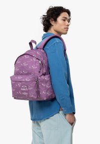 Mochila morada con estampados que presentan personajes de dibujos animados, asa superior, dos correas para los hombros y un bolsillo frontal marcado "Eastpak".