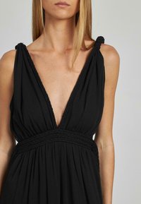 Vestido negro sin mangas con un profundo escote en V, detalles trenzados en la cintura y tejido texturizado, que presenta suaves drapeados y tirantes ajustables anudados.