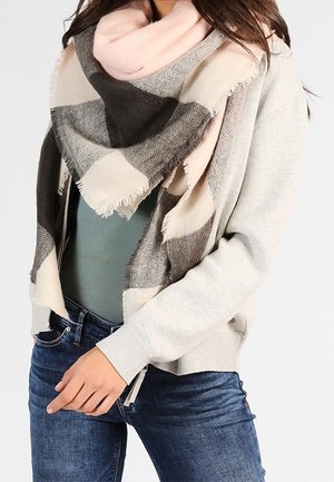 Femme portant une grande écharpe à carreaux rose, grise et beige sur un cardigan gris, une chemise bleu sarcelle et un jean bleu.