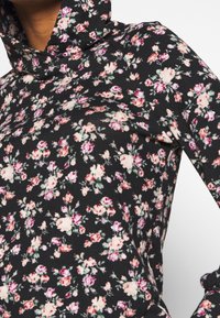 Haut noir à manches longues avec un col bénitier, présentant un motif floral en rose et vert. Confectionné en tissu doux avec une coupe ajustée.