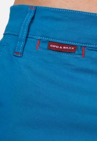 Blauwe stoffen shorts met rode stiksels, voorzien van een labeltje met de tekst "CIPO & BAXX" nabij de tailleband.