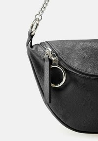 Bolso de mano negro con textura, de forma curva, con herrajes plateados, cierre de cremallera y correa de cadena. Presenta un anillo metálico redondo y un fleco de cuero.