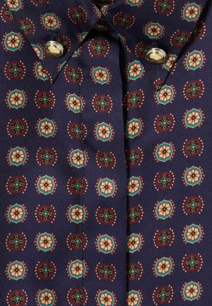 Femme portant une chemise boutonnée à motifs, un jean bleu clair, des bottes noires montantes et tenant un sac à bandoulière noir.