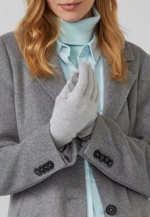 Graue Wollhandschuhe mit strukturiertem Strickmuster, getragen von einer Person in einem grauen Mantel und einem hellblauen Hemd, die Hände zusammengelegt.