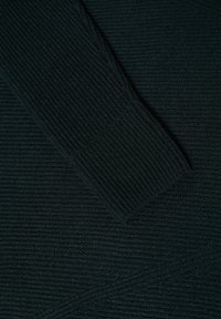Svart ribbat stickad tyg med en texturerad yta, långa ärmar och vinklade sömmar. Materialet verkar mjukt och lätt.