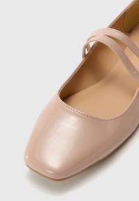 Ljusrosa lacklacksballerinor med fyrkantad tå och två smala remmar över fotleden. Slät yta med vadderad innersula.