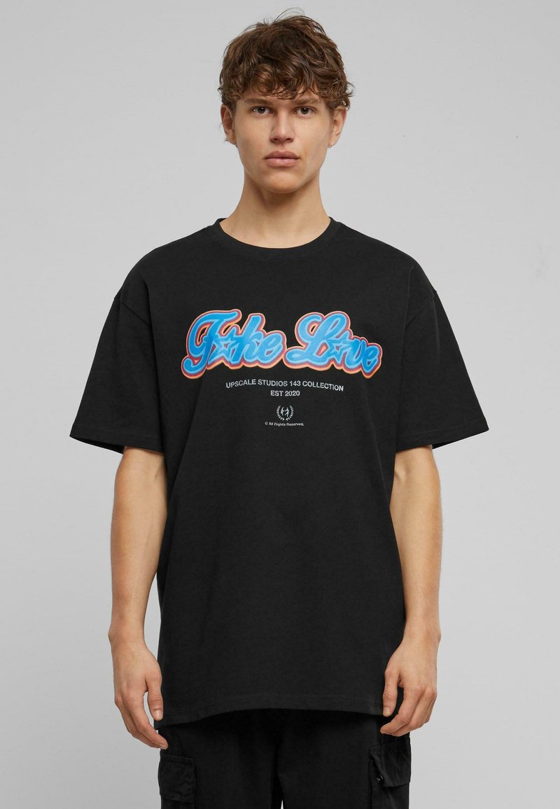 Svart oversized T-skjorte laget av bomull. Har fargerik grafisk tekst "Fake Love" i blått og rødt med stjerneakcent, sentrert på brystet.