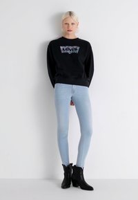 Melna svītra ar Levi's logotipu, gaiši zila šaurā džinsu bikses un melnas potītes zābaki. Gluda auduma, pieguloša dizaina, ar ikdienišķu izskatu.
