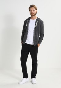 Grå hettejakke med hvite snorer, brukt over en hvit T-skjorte, kombinert med svarte bukser og hvite sneakers; avslappet stil.