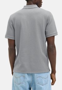 Grå polo shirt med struktureret stof, korte ærmer og ribbet krave. Bæres med lyseblå denim jeans.