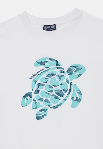 Camiseta blanca con un gráfico estilizado de una tortuga marina en azul y verde azulado, y una etiqueta marina que dice "Vilebrequin" en el cuello.