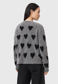 Maglione grigio lavorato a maglia con motivi a cuore neri in rilievo. Maniche lunghe, scollatura tonda, vestibilità rilassata e tessuto testurizzato.