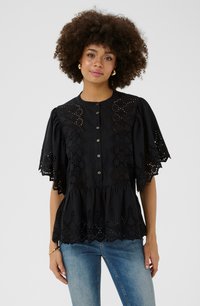 Schwarze Baumwollbluse mit filigranen Lochdetails, kurzen, ausgestellten Ärmeln, einer durchgehenden Knopfleiste und einem Peplum-Saum. Kombiniert mit blauen Jeans.
