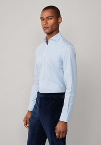 Camicia azzurro chiaro con un motivo sottile e maniche lunghe, abbinata a pantaloni in velluto a coste blu scuro con passanti per cintura.