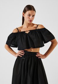 Crop top nero scollato con maniche a volant, caratterizzato da un'apertura a occhiello e spalline sottili, abbinato a una gonna nera coordinata.