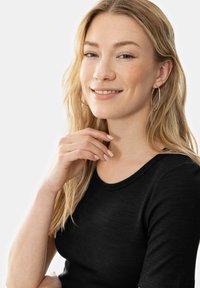 Černé žebrované tričko s kulatým výstřihem. Modelka má vlnité blond vlasy a stříbrné kruhové náušnice, na neutrálním pozadí.