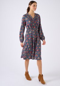 Abito a maniche lunghe con scollo a V, caratterizzato da un motivo floreale in rosso, giallo e blu su uno sfondo scuro, stretto in vita.