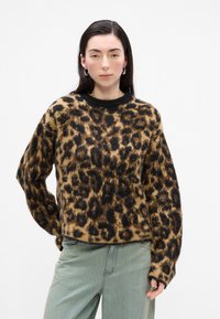 Svetr s leopardím potiskem v odstínech hnědé a černé, měkká textura, volný střih, hřejivý černý lem u krku, spárovaný se světle modrými džíny.