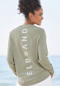 Langarmshirt in Olivgrün mit weißem Text "ELBSAND" senkrecht auf dem Rücken, mit lässigem Schnitt und weicher Stoffbeschaffenheit.