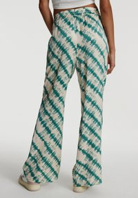 Ausgestellte Hosen in hellbeige mit einem türkisfarbenen Batikmuster. Mit einem elastischen Bund und weichem Stoffgefühl.