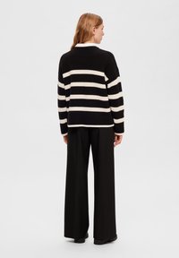 Maglione a righe nero e crema con scollo rotondo e vestibilità ampia, abbinato a pantaloni neri a vita alta. Nessun motivo o accento notevole.
