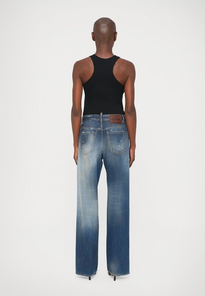 Pantalones vaqueros de denim azul con un acabado desgastado, ajuste recto y parche de cuero en la parte trasera de la cintura; combinados con una camiseta sin mangas negra.