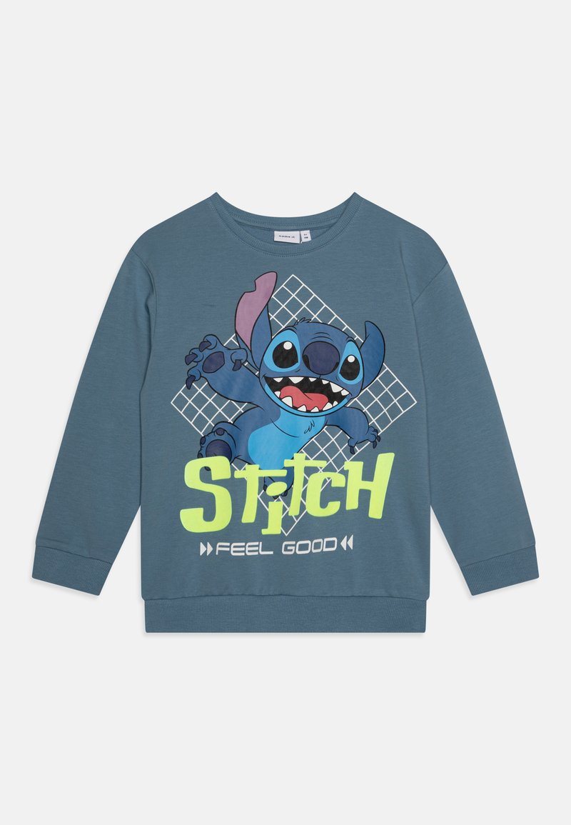 Sweat-shirt à manches longues bleu avec un personnage de cartoon, Stitch, accompagné du texte graphique "FEEL GOOD" en jaune vif et d'un fond à motif de grille.