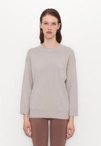 Lys grå genser med teksturert rutemønster, rund hals og 3/4-ermer, laget av et mykt strikkemateriale, noe oversized passform.