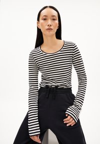 Gestreiftes langärmeliges Oberteil in Schwarz und Weiß mit rundem Ausschnitt und ausgestellten Ärmelbündchen, kombiniert mit schwarzen Hosen mit Kordelzug-Taillierung.