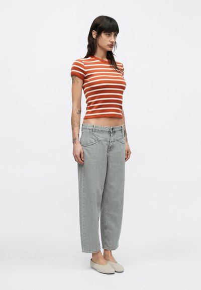 Ριγέ, εφαρμοστό τοπ σε πορτοκαλί και λευκό, συνδυασμένο με φαρδιά, ανοιχτογκρι τζιν. Το σύνολο ολοκληρώνουν μπεζ παπούτσια που φοριούνται χωρίς κορδόνια.