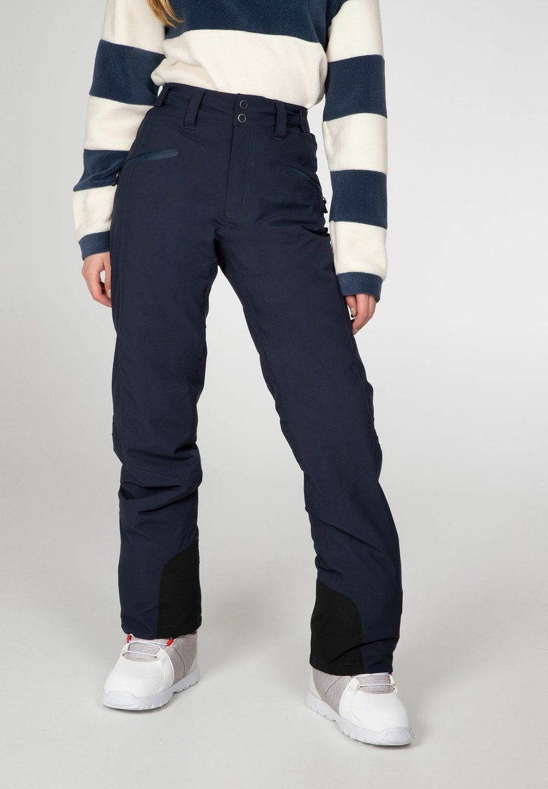 Pantalons de ski bleu marine à coupe ajustée, dotés de poches zippées, de jambes inférieures renforcées et d'accents en tissu noir au niveau des chevilles.