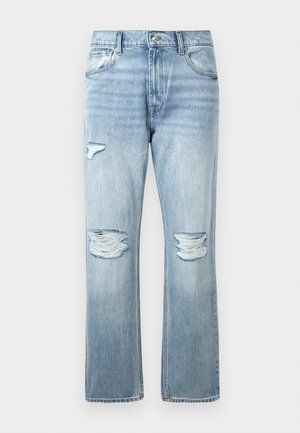 Jeans de denim azul claro con desgarros distanciados en ambas rodillas y un pequeño desgarro en la parte superior del muslo izquierdo, estilo clásico de cinco bolsillos.