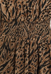 Leopardmönstrad klänning i nyanser av brunt och svart. Har ett smockat midja för flexibilitet och en svängande kjol med texturerad tyg.