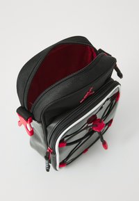 Borsa nera con zip e accenti rossi, superficie texturizzata e design elastico a bungee. Interno rosso, con due scomparti e zip robuste.